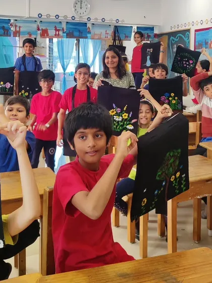 A vibrant classroom full of young students joyfully holding up tote bags they've painted with unique floral designs. This image captures the energy of a school workshop and the pride of creating a beautiful, usable piece of art.