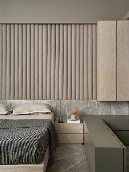 This versatile guest room features a custom bed with a channel-tufted headboard set against a backdrop of grey marble and upholstered wall panels. The monochromatic palette simplifies the design, allowing the different textures to stand out.