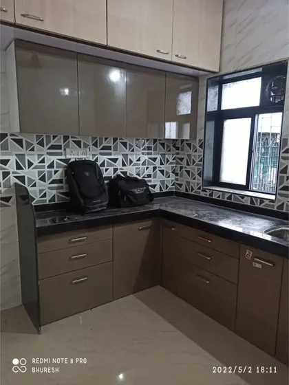 This kitchen in Bhayander showcases high-gloss laminate cabinets and a striking geometric tile backsplash. Even in a standard layout, the right materials can create a modern and fresh look.