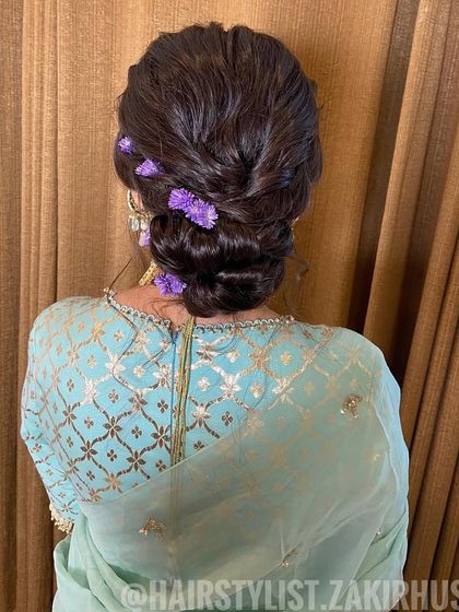 A classic low bun with a side braid, decorated with purple flowers. This is an elegant and understated look, ideal for a wedding guest or for a smaller, intimate function.