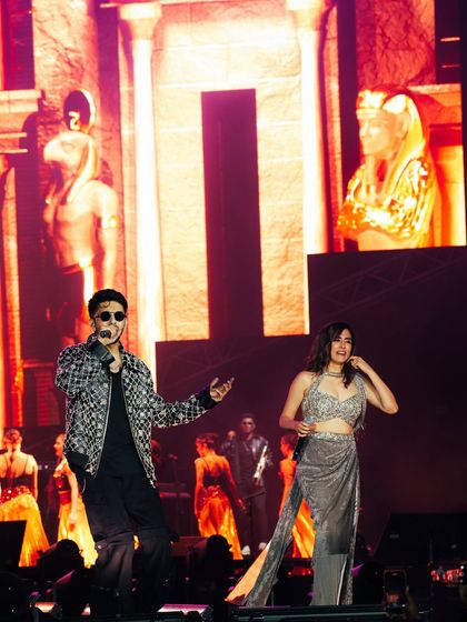 Anirudh Ravichander and Jonita Gandhi sharing the stage during the Hukum Tour in Bangalore, with massive Egyptian-themed visuals behind them.