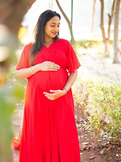 The vibrant red of her dress stands out beautifully against the soft green of the park. This solo maternity portrait showcases how choosing the right outfit can add a pop of color and energy to your outdoor photoshoot.