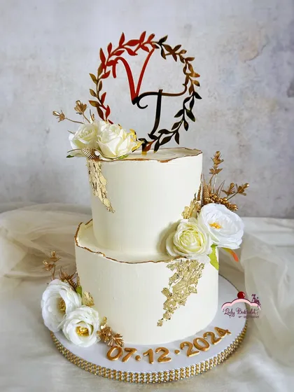 Gold accents and love-filled layers. An elegant two-tier engagement cake in ivory and gold, adorned with white roses and a custom monogram topper.