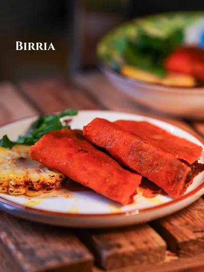 A plate of rich, slow-cooked Mexican Birria, served with a side of grilled corn.