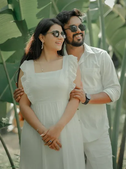 A fun and carefree moment captured against a backdrop of lush tropical leaves. The couple, dressed in matching white, shares a laugh, showcasing the relaxed and joyful side of their relationship.