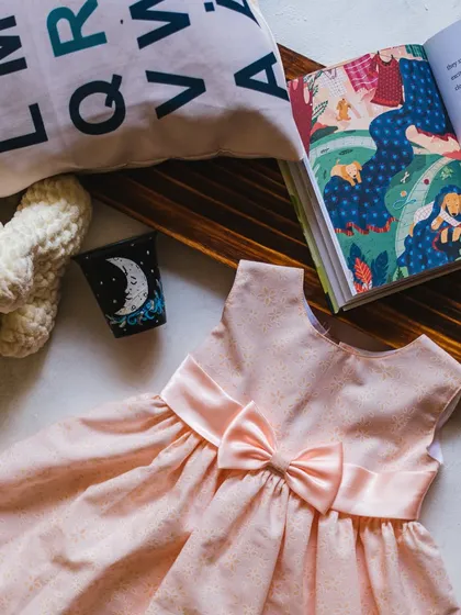 A simple and sweet peach-colored dress with a subtle print. The main feature is the large, beautifully tied satin bow that gives it a classic, elegant feel.