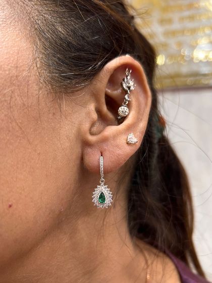 An elegant stack featuring a green gemstone drop from the lobe and a delicate hanging from the helix.