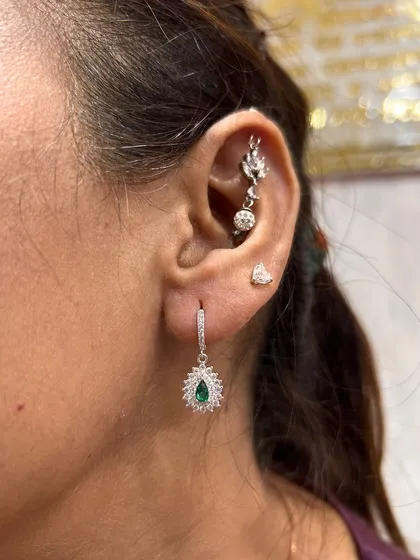This elegant ear features a stunning emerald-green teardrop earring, perfectly complemented by a delicate silver hanging and a simple tragus stud.