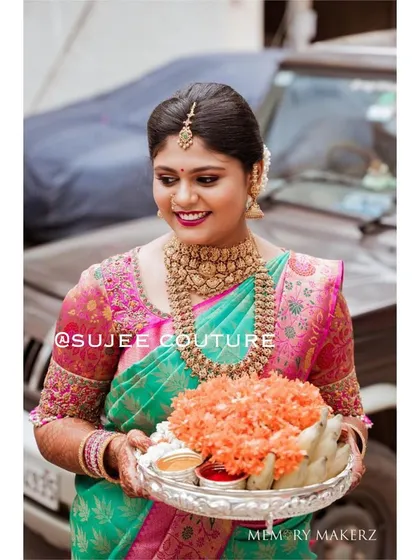 A client looking lovely during a traditional ceremony. Her green and pink silk saree is paired with a custom blouse featuring intricate embroidery on the sleeves, adding a personal touch to her festive wear.