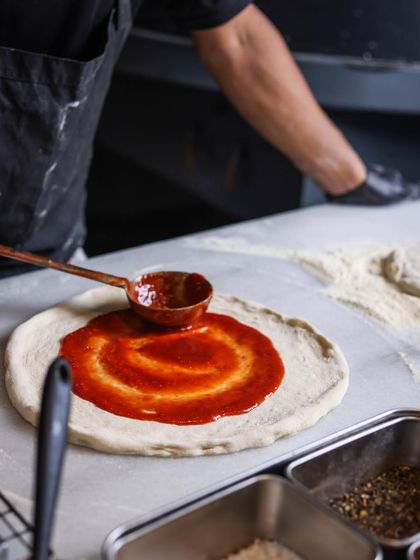The secret sauce. Spreading the rich tomato sauce is a meditative and essential part of the pizza-making process.