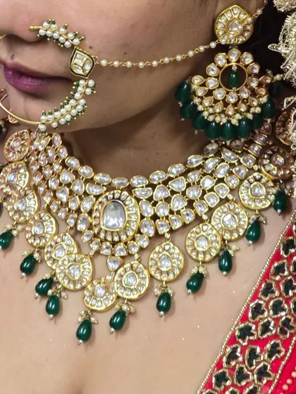 A close-up of a beautiful Pachi Kundan necklace with green bead drops, worn with a red lehenga. The detail in the Kundan work is clearly visible.