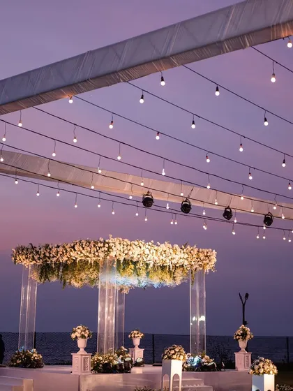 The full view of a spectacular sundowner reception setup in Goa. The mandap glows under a canopy of fairy lights as the sky turns a beautiful shade of purple, creating an unforgettable evening atmosphere.