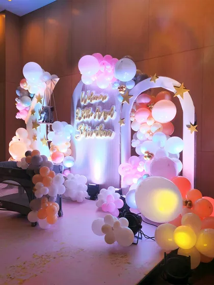 The main decor setup for the baby arrival party, featuring a baby cot, balloon clouds, and illuminated arches. The soft lighting and pastel colors create a sweet and dreamy atmosphere.