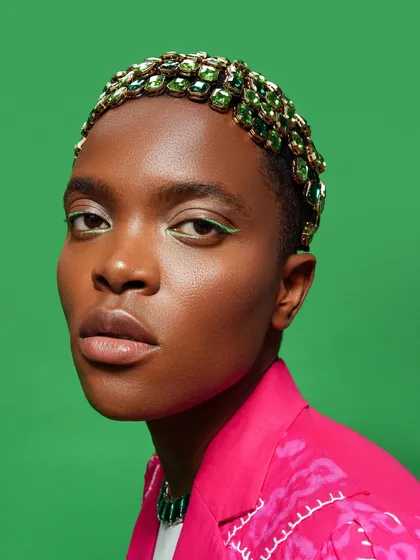 A detailed shot of the emerald green bejeweled hair and matching graphic liner. This shows the precision required for both the makeup and the hairpiece application.