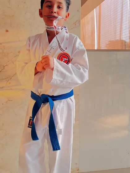 A young student proudly bites his bronze medal after his first tournament attempt. This moment captures the joy of achievement and the start of his competitive journey.