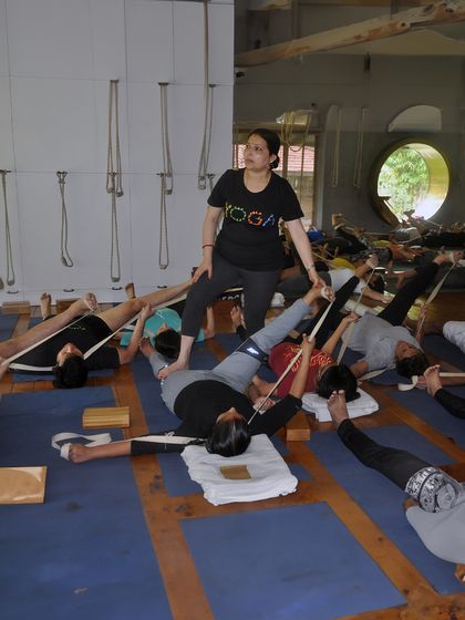 A class of students using belts for leg stretches. This is a fundamental practice in Iyengar yoga to improve hamstring flexibility and relieve lower back pain.