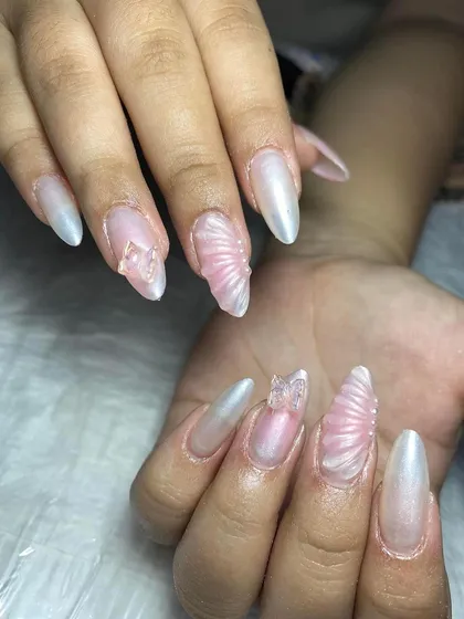 Pearlescent nails with sculpted shell textures and butterfly charms. This design captures the 'mermaidcore' trend perfectly.