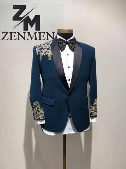 A teal blue tuxedo with a classic black satin lapel, accented with beautiful gold floral embroidery on the shoulder and cuff. A perfect fusion of Indian motifs and Western tailoring.