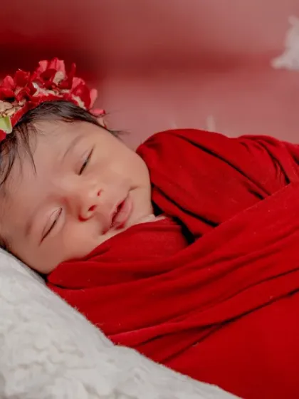 A smile as bright as a flower. This baby, wrapped in red, is sleeping soundly with a beautiful floral crown.