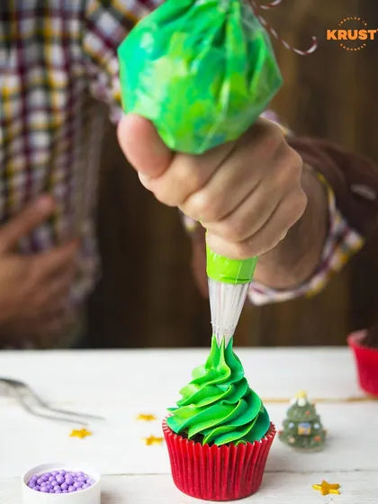 A close-up of a cupcake being frosted with vibrant green icing. In our workshops, you'll get hands-on practice with piping bags and different decorating styles.