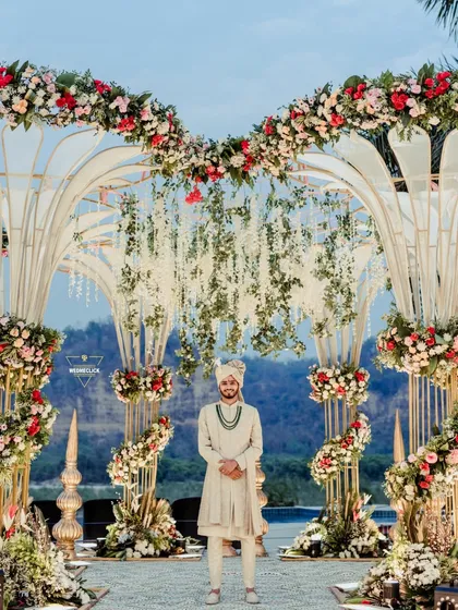 The groom stands proudly at the mandap, awaiting his bride. The stunning floral decor and scenic backdrop make this a truly grand portrait.
