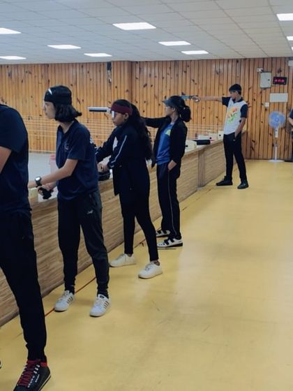 Students practice their 10-meter pistol shooting stances in a line. This image captures a typical training day where shooters work on consistency and aim under supervision.