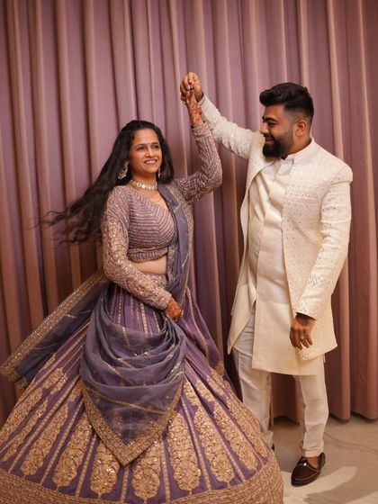 A couple dancing, with the woman wearing the beautiful mauve-purple lehenga.