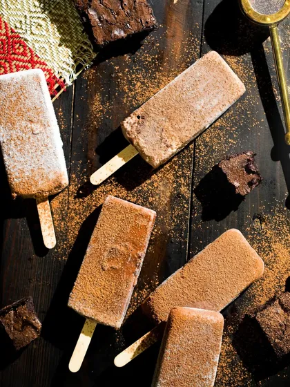 A top-down shot of chocolate fudge popsicles and brownie pieces on a dark wooden surface, creating a rich and decadent mood.