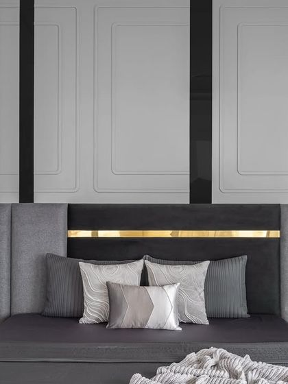 The master bedroom exudes calm sophistication. We chose soft grey walls and a striking black and grey headboard with a gold accent to serve as a bold focal point, complemented by elegant wall paneling.