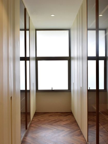 This image shows a galley-style walk-in closet we designed to maximize a narrow space. We used mirrored and fluted panel doors to create a sense of depth and texture.