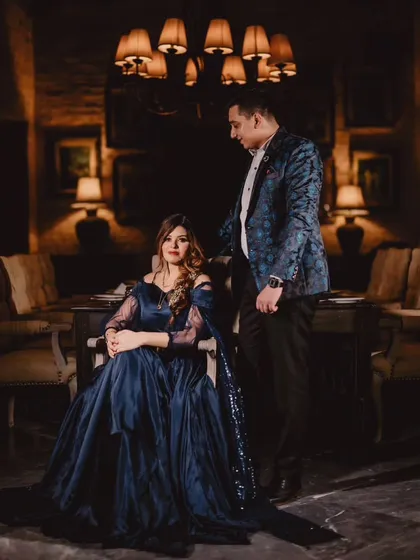 A moody and elegant portrait in a dimly lit, luxurious setting. The navy blue gown with its sequined trail adds a layer of sophistication and drama.