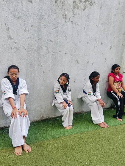 Students hold the wall sit pose, building isometric strength in their legs. This is a key conditioning exercise for developing a powerful Taekwondo stance.
