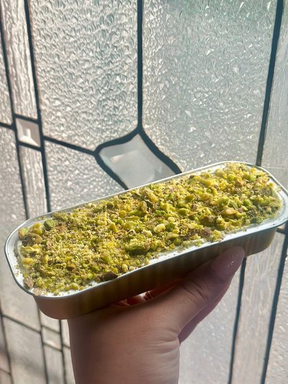 A freshly baked pistachio-crusted loaf cake, held up to the light. This image captures the delicious texture and homemade quality of our bakes.