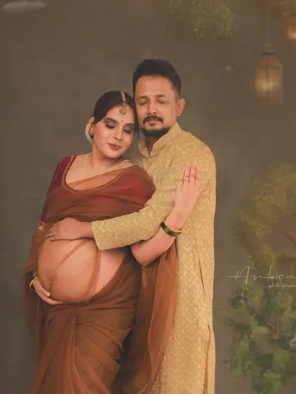 An intimate moment between the couple, captured within a rich, painterly setting. This portrait focuses on their connection, with the traditional attire and artistic backdrop adding layers of cultural depth and warmth to their maternity story.