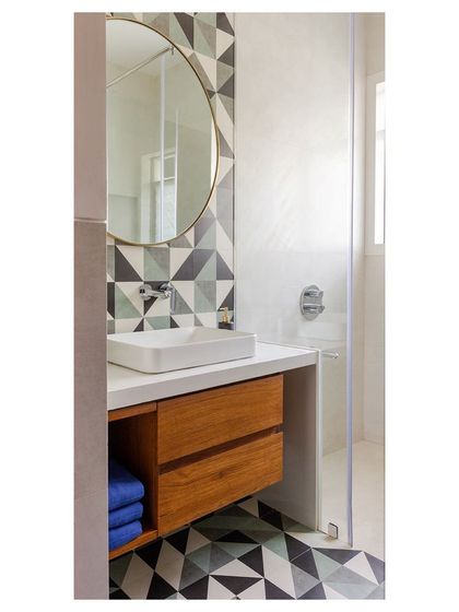 This bathroom features bold geometric tiles on the floor and wall, creating a playful yet sophisticated graphic pattern. The design combines a floating wooden vanity and a large circular mirror to maximize the sense of space in a compact area.