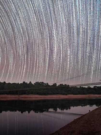 Star trails reflect over a hanging bridge in the Western Ghats. This image is composed of hundreds of photos to show the Earth's rotation against the backdrop of the night sky.