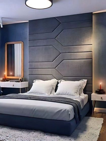 This bedroom features a striking geometric-paneled accent wall in a deep blue. The design is complemented by a matching blue bed frame and a simple vanity table, creating a modern and moody atmosphere.