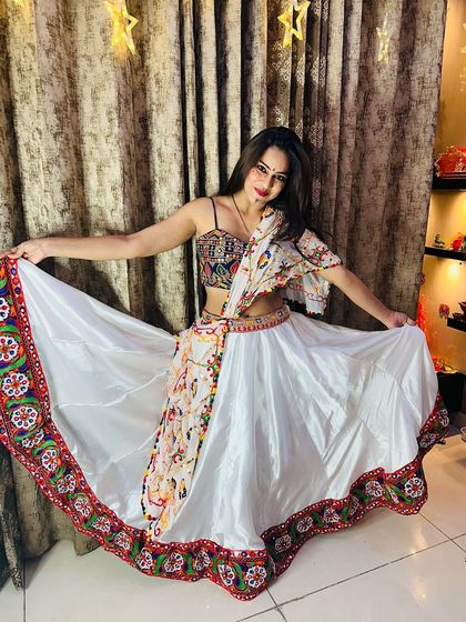 A beautiful white satin lehenga with a colorful embroidered border. The multi-color mirror work blouse and printed dupatta make it a standout piece for Garba.