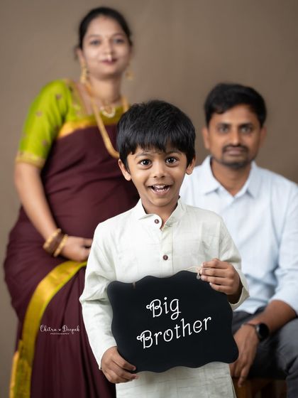 A proud big brother holds a sign announcing his new role, with his expecting parents looking on from the background in this heartwarming family maternity photo.