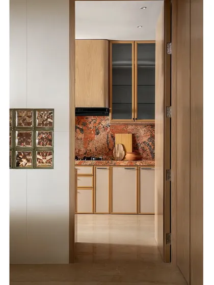 A view into the kitchen through the doorway, showing how the glass blocks on the outer wall allow light to filter in. The warm wood and bold marble create an inviting and visually interesting kitchen.