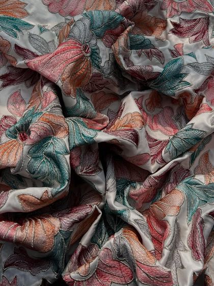 A close-up of our embroidered satin, showing the intricate, multi-colored threadwork that creates a stunning floral pattern. This fabric is a work of art.
