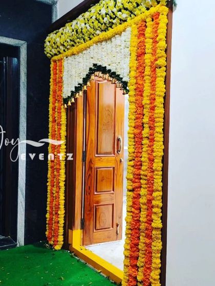 A traditional housewarming door decoration using garlands of orange and yellow marigolds and white jasmine. This classic design brings a festive and auspicious feel to your new home's entrance.
