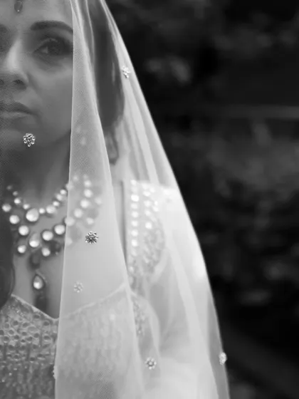 A close-up black and white portrait of the bride, her face partially covered by her veil, creating a sense of mystery and elegance.
