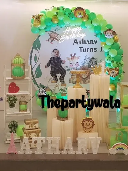 A jungle theme with a personalized backdrop featuring the birthday boy's photo. The green balloon arch and animal cutouts create a fun and personal celebration.