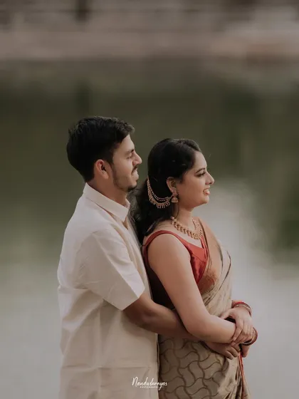 A couple stands by the water, the groom embracing the bride from behind as they both look out at the view, creating a calm and connected portrait.