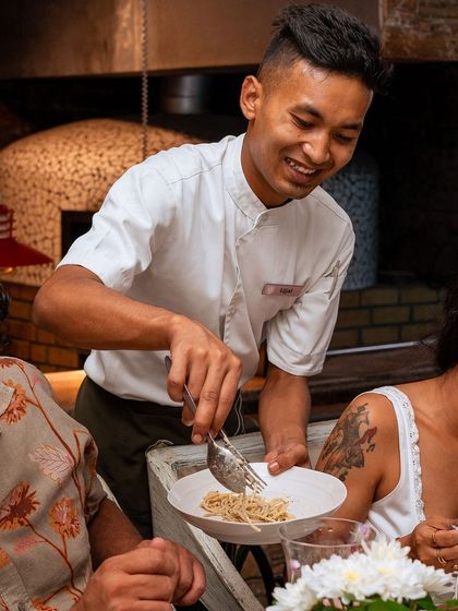 A member of my service team carefully serves a plate of fresh pasta, embodying the attentive and warm hospitality of Roxie.