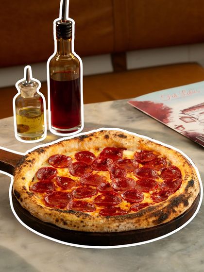 A clean shot of our classic pepperoni pizza served on a wooden paddle, with bottles of chili and olive oil ready for drizzling.