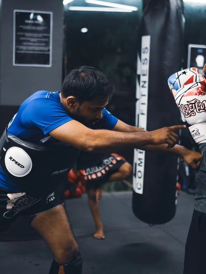 A coach points out a target during a pad work session. This drill sharpens a fighter's accuracy and teaches them to aim for effective scoring areas.