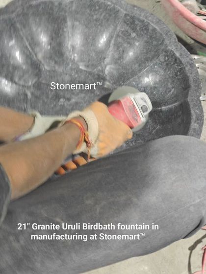 An artisan is polishing the inside of a 21-inch granite uruli birdbath. This finishing process ensures a smooth surface and brings out the stone's natural luster.