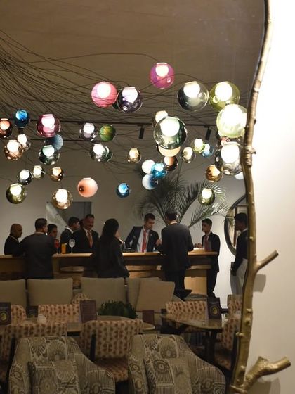 A reflection of the Bocci 28 series installation in a mirror, showing the lights within the context of the bustling VIP lounge at the India Art Fair.